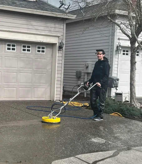 The owner pressure washes a driveway with a circular surface cleaner attachment.
